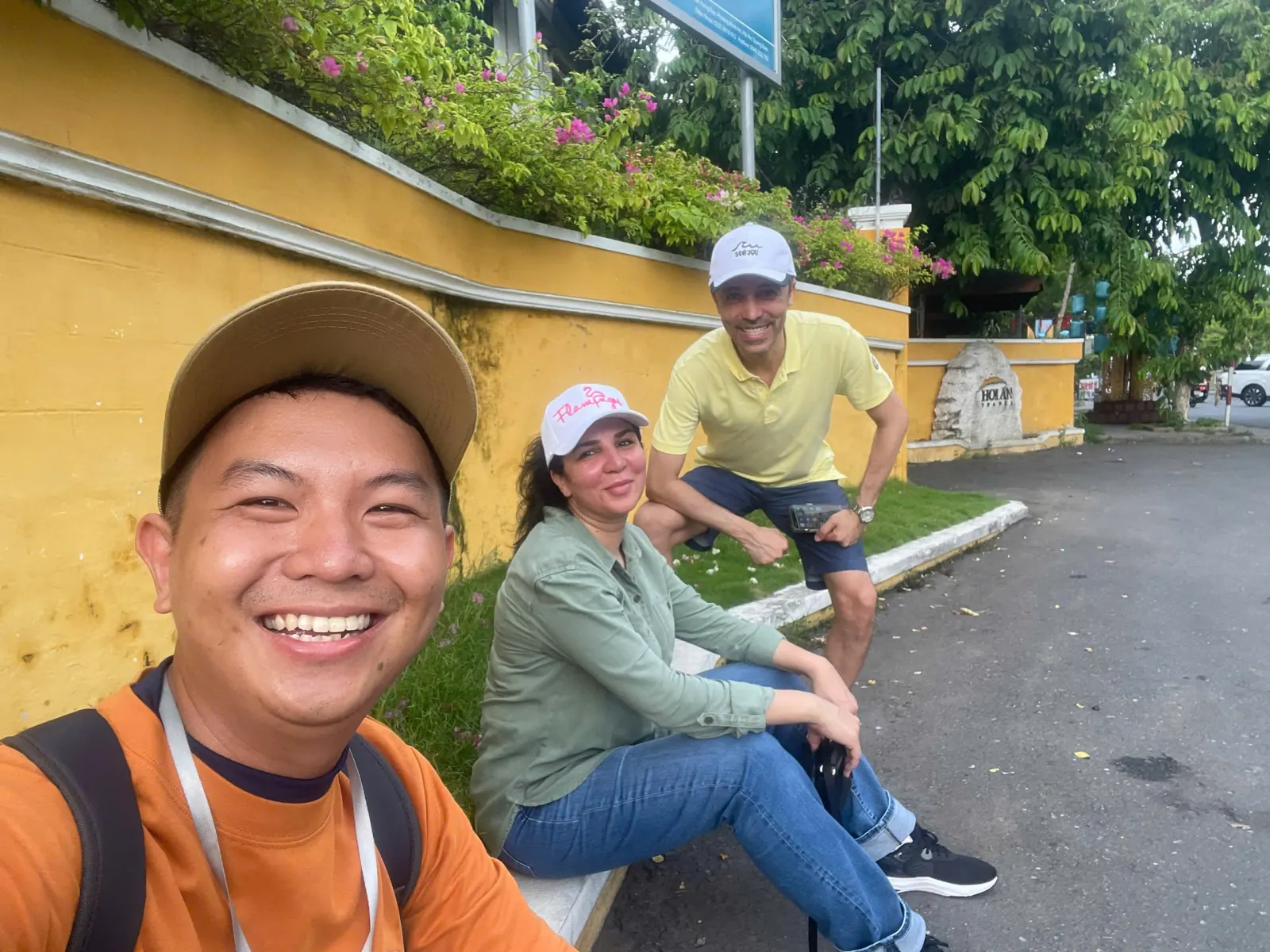 A couple resting against the yellow wall of Hoi An Ancient Town with their guide