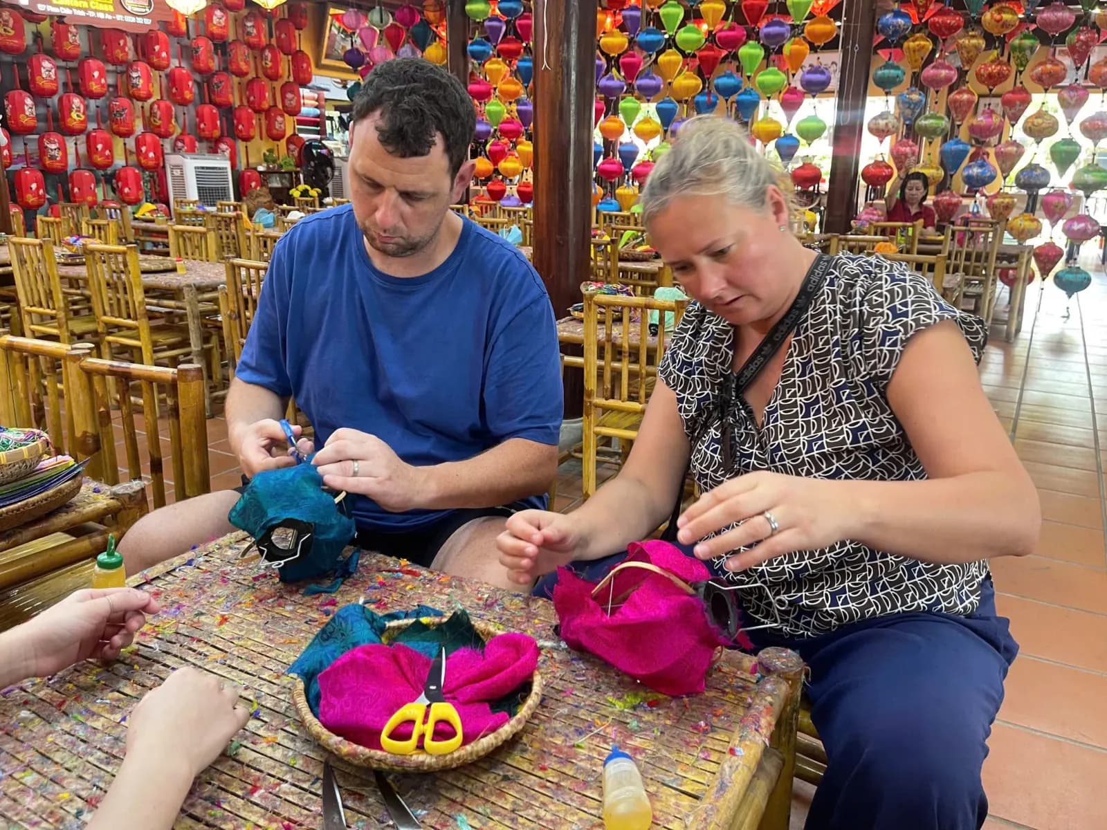 Two guests making silk lanterns in a Hoi An workshop under rows of finished lanterns