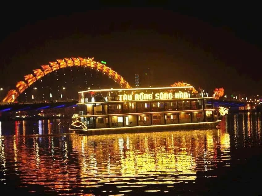 A lit dragon boat on the Han River in front of the illuminated Dragon Bridge at night
