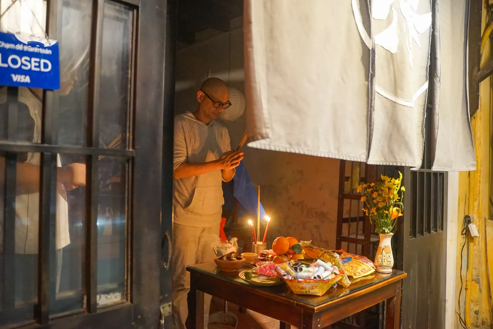 Restaurant owner prays with incense at a Tet altar in Hoi An, warm candlelight and offerings in frame