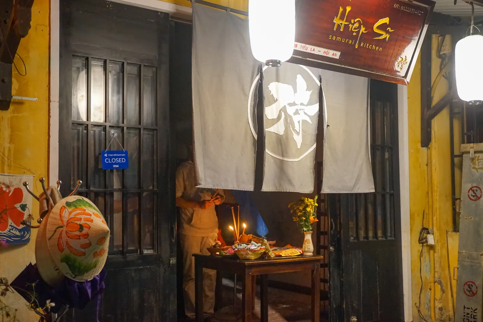 Pavement offering table outside a closed Hoi An restaurant on Tet eve, lit by a single lantern