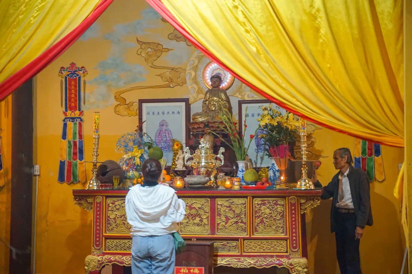 Visitor standing before the temple altar with its Buddha statue, fruit and flower offerings on Tet eve