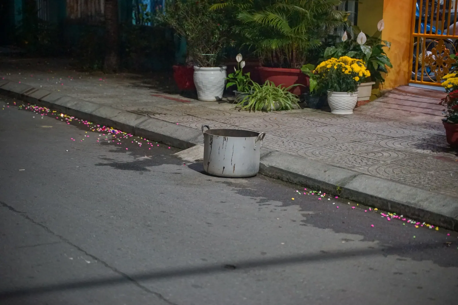 Aluminium pot left at the kerb after burning offerings, with lucky confetti scattered across the street