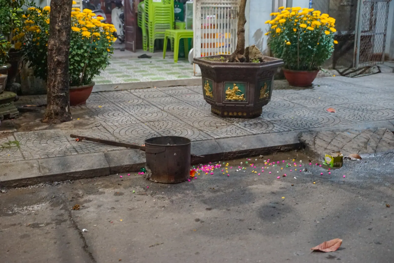 Metal burner on a Hoi An pavement after the joss paper was burned, confetti and pots of yellow chrysanthemum around it